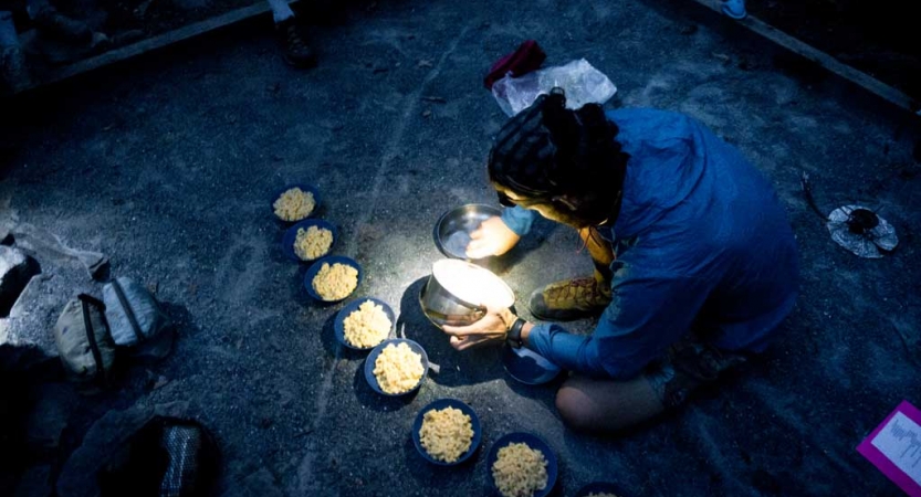 A person prepares bowls of food by headlamp 